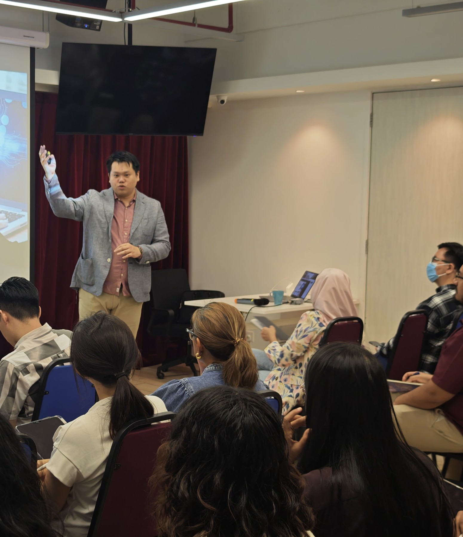 Aaron at the front of a training room with one hand raised, explaining a point to rows of seated attendees